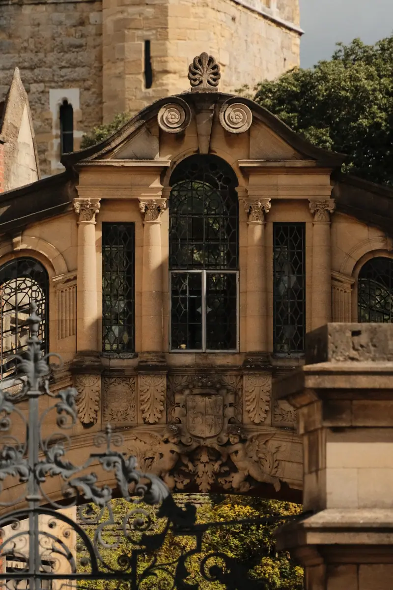A carved baroque gateway in honey-coloured stone behind black iron railings