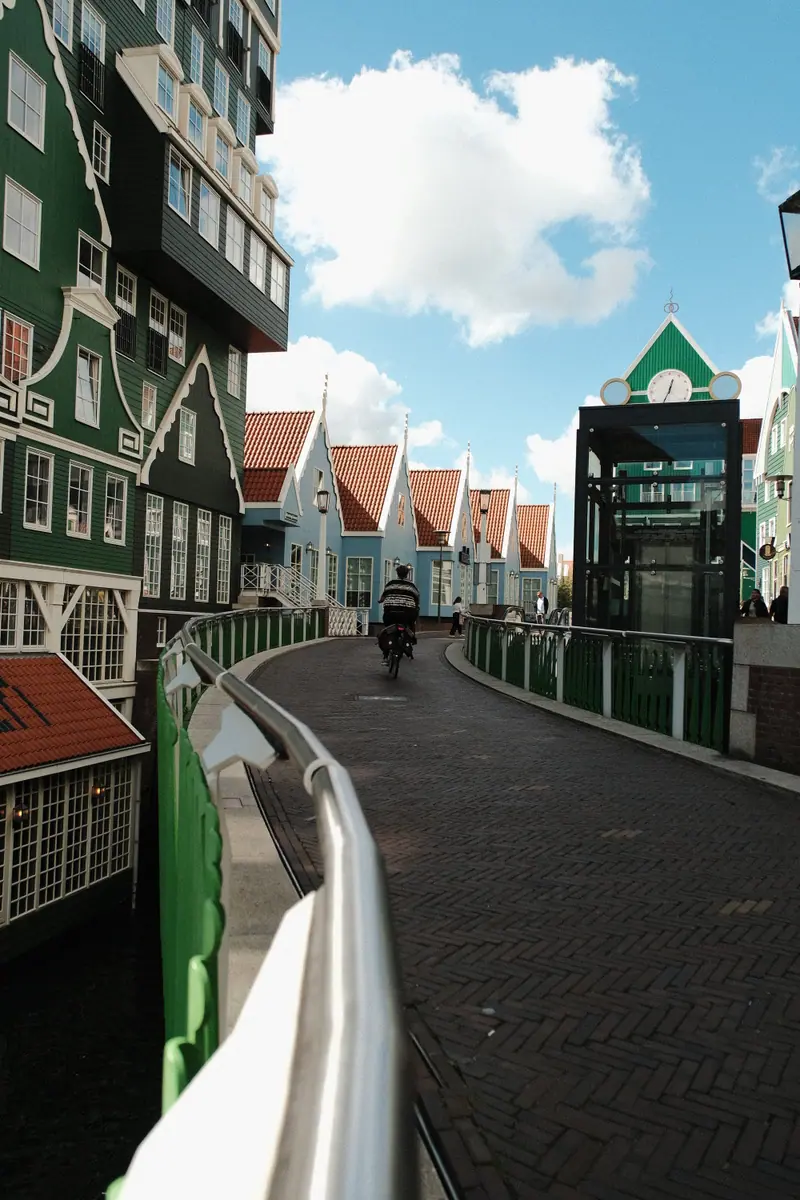 A cyclist rides between stacked green Zaan-style houses under a bright sky