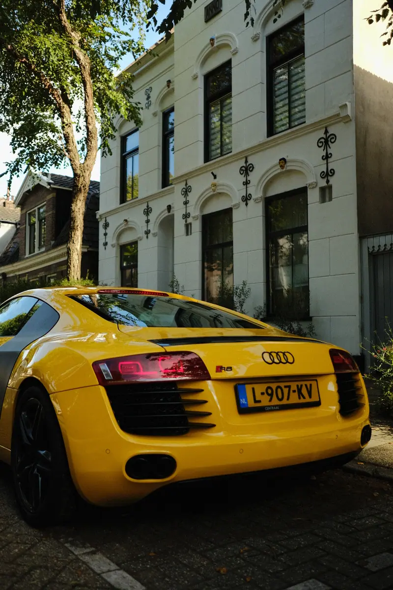 A yellow Audi R8 parked on a cobbled street in front of a white townhouse