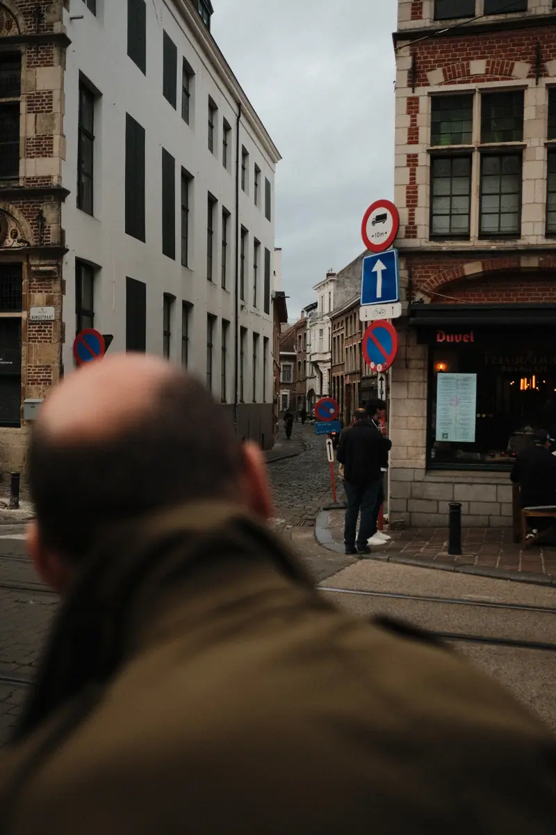Looking past the back of a man's head down a street of brick and white facades