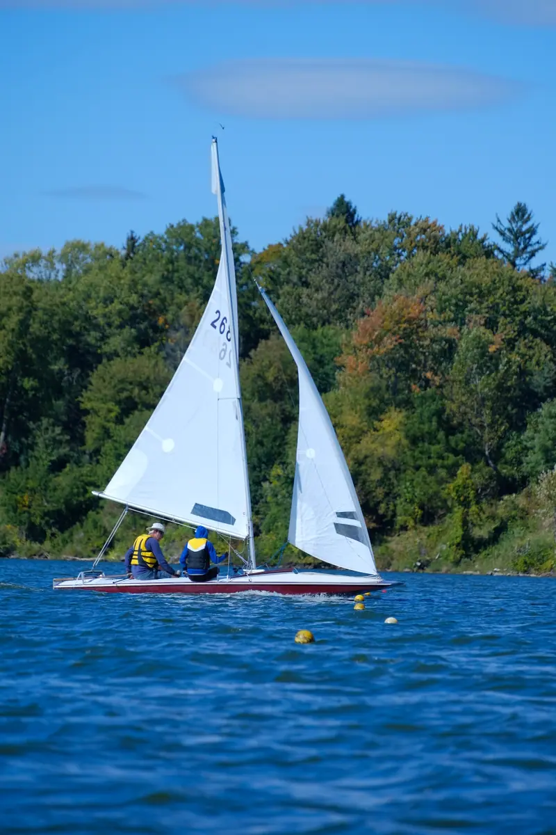 Two people sail a small white sailboat on the lake