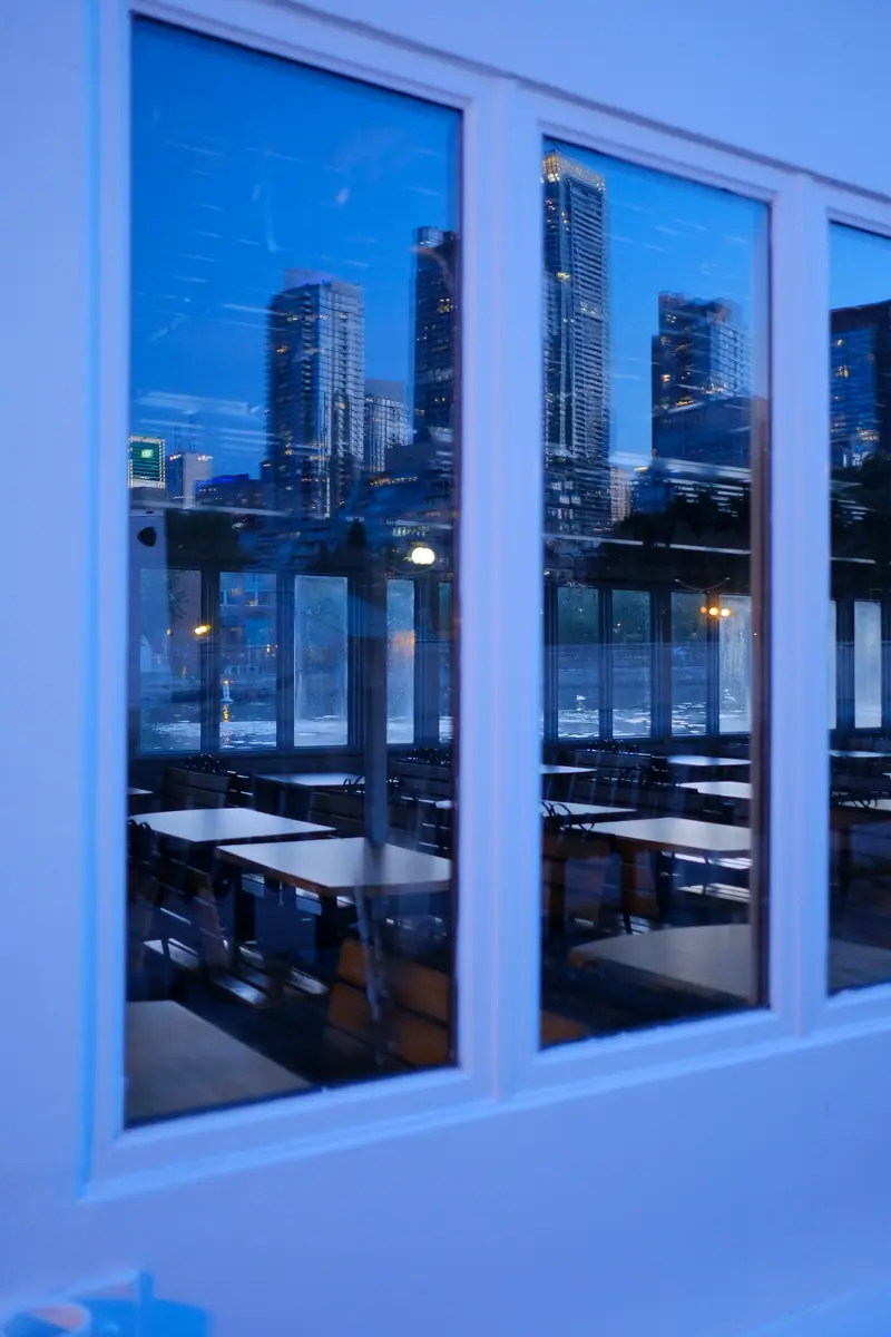 Toronto's towers reflected in the windows of a moored boat's empty dining room at blue hour