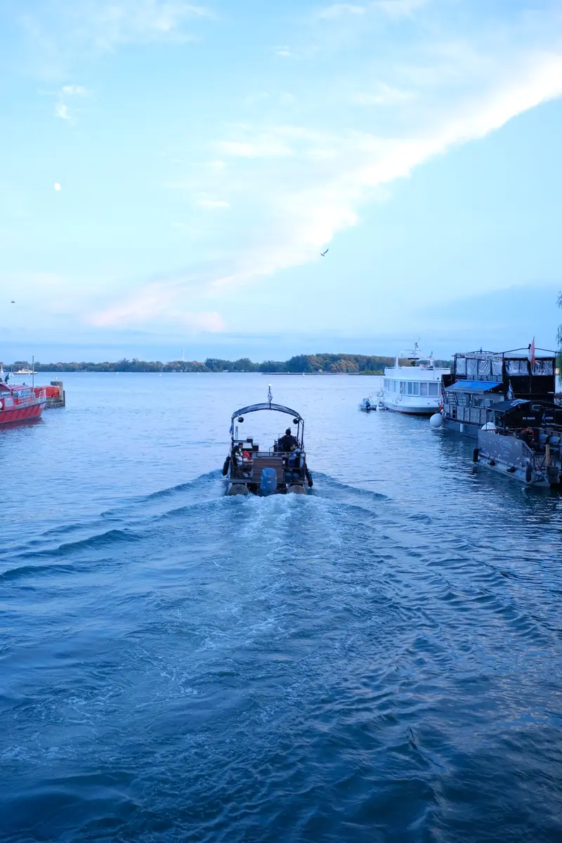 A small boat leaves a long wake across the harbour toward the islands at dusk