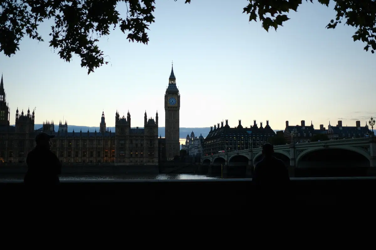 Westminster in silhouette against the evening sky, framed by leaves