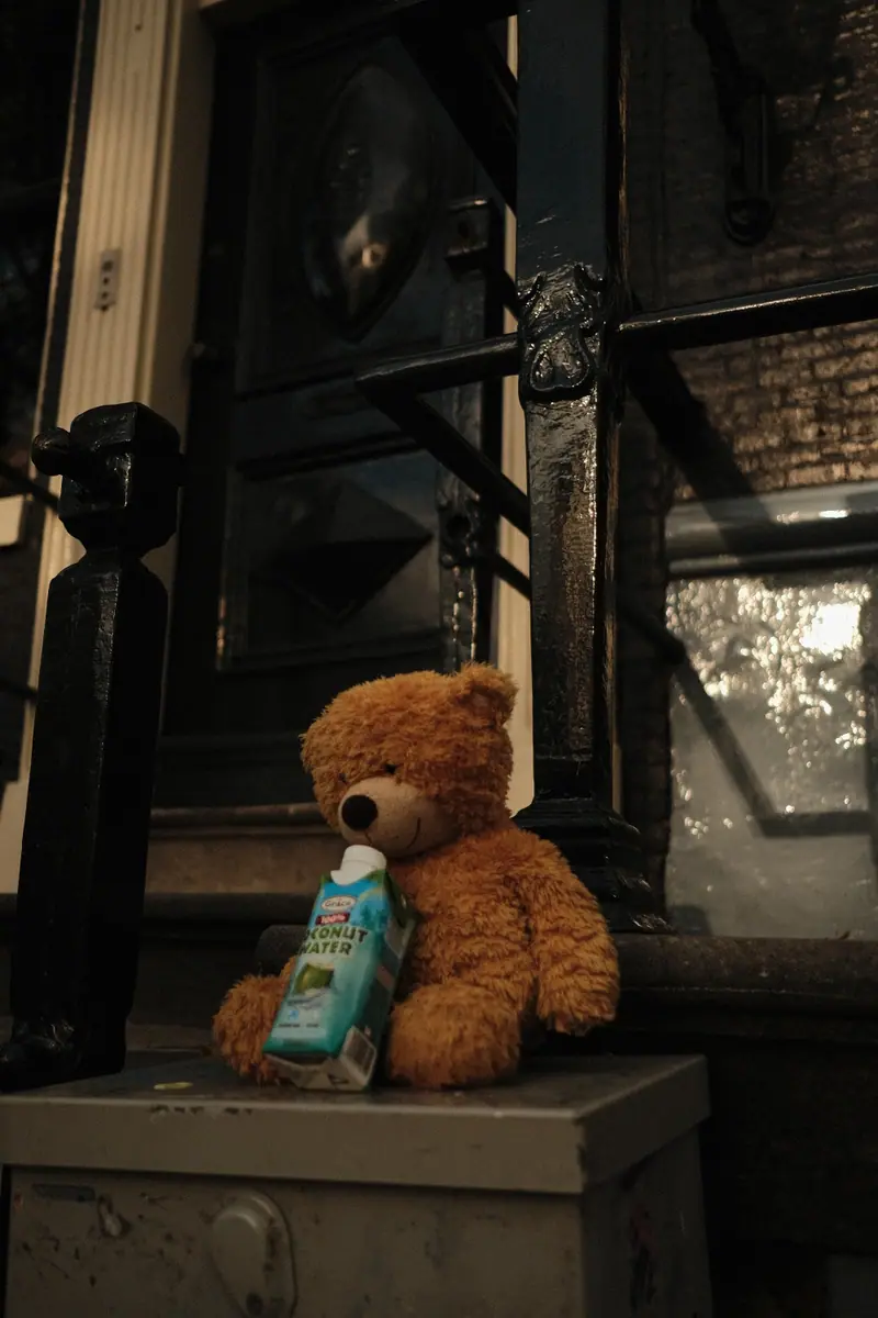 A teddy bear holding a drink carton sits on a ledge in an old doorway
