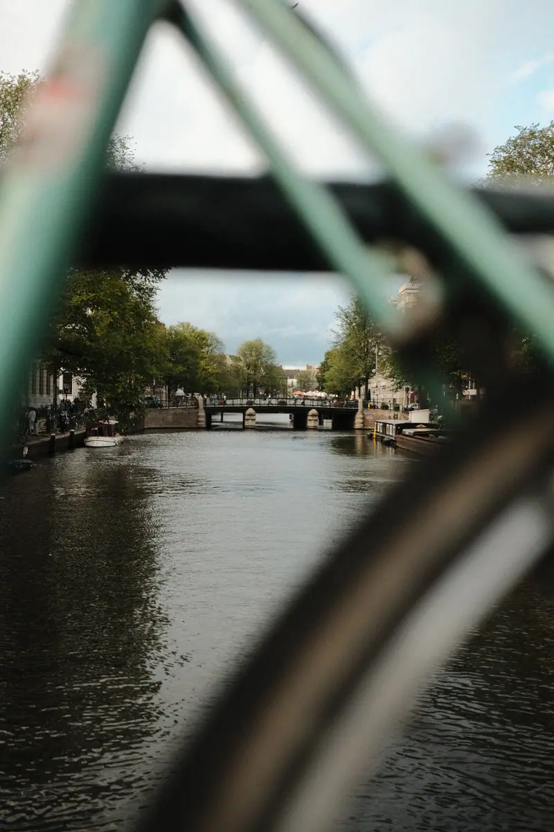 An Amsterdam canal and bridge seen through the green frame of a parked bike