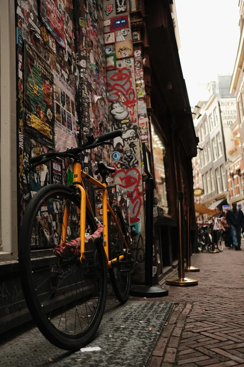 A yellow bike leans against a sticker-covered wall in a narrow Amsterdam street