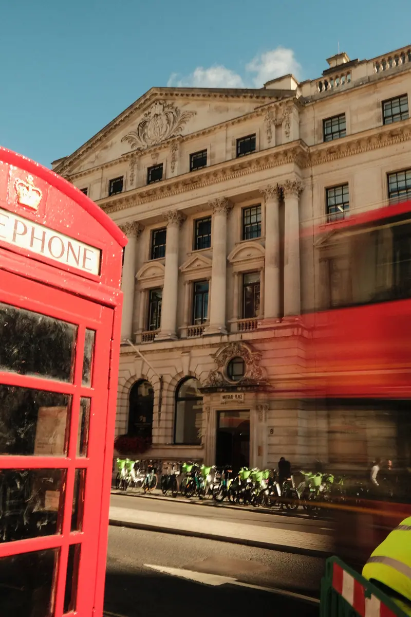 A red phone box and a passing red bus in front of a grand stone building
