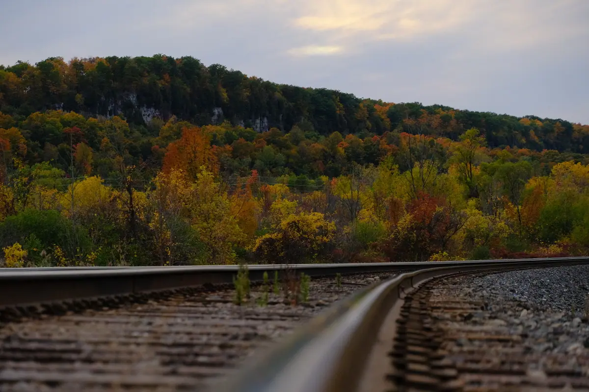 A curving railway track runs toward an autumn ridge