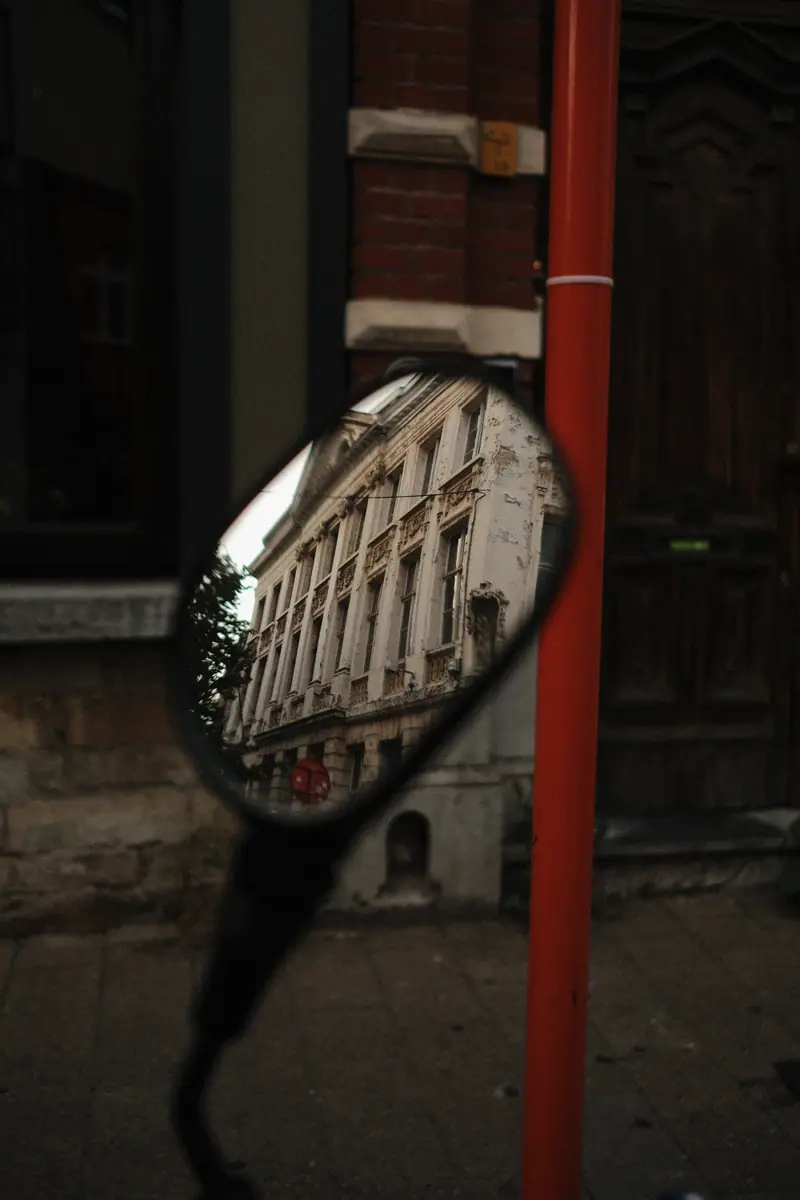 A scooter mirror reflecting an ornate building, beside a red pole