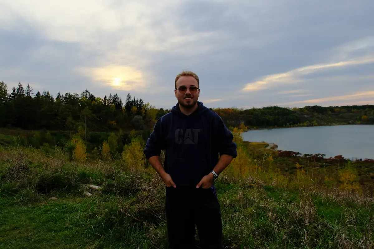 Hamza standing in tall autumn grass at Rattlesnake Point, a quarry lake and the evening sky behind him