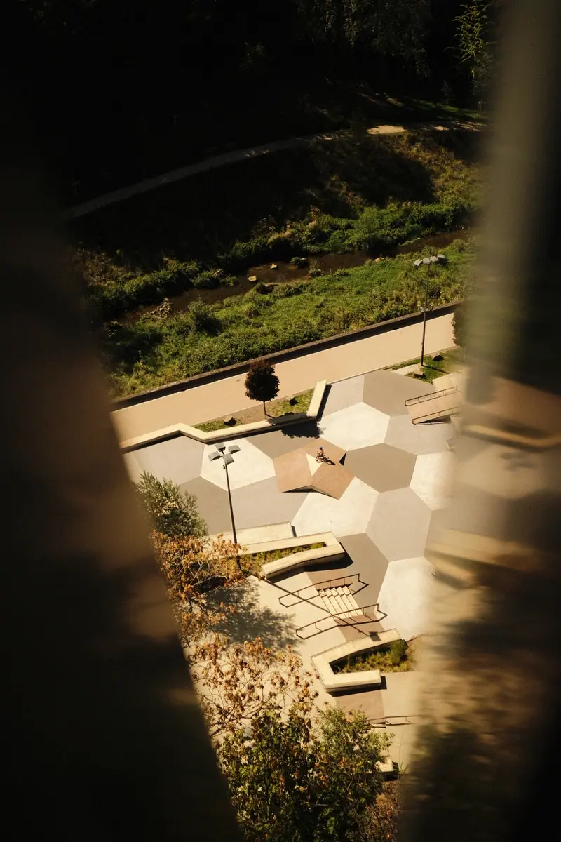 Looking down through a gap at a sunlit park of hexagonal paving