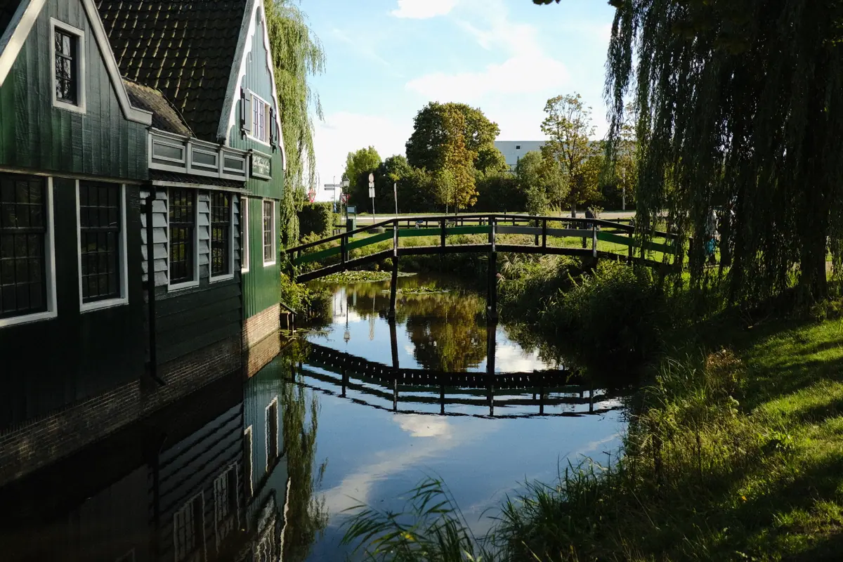 Green wooden houses and an arched footbridge reflected in still water