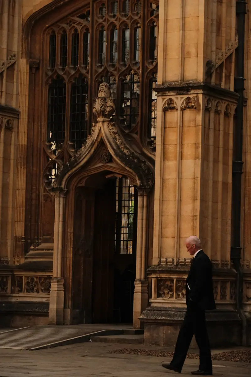 A man in a dark suit walks past an ornate Gothic doorway in golden stone