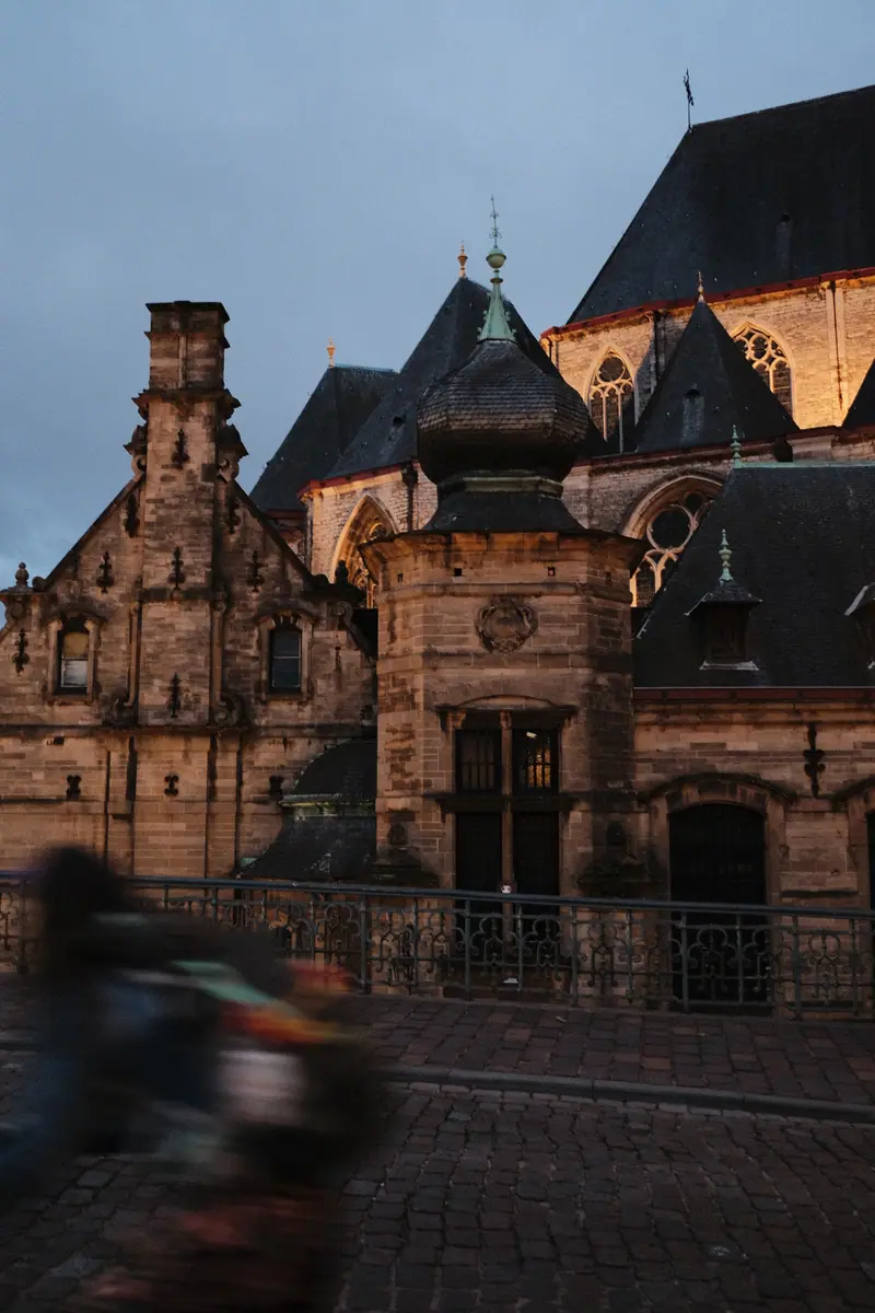 A Gothic cathedral and a gabled hall lit by evening sun, a cyclist blurring past
