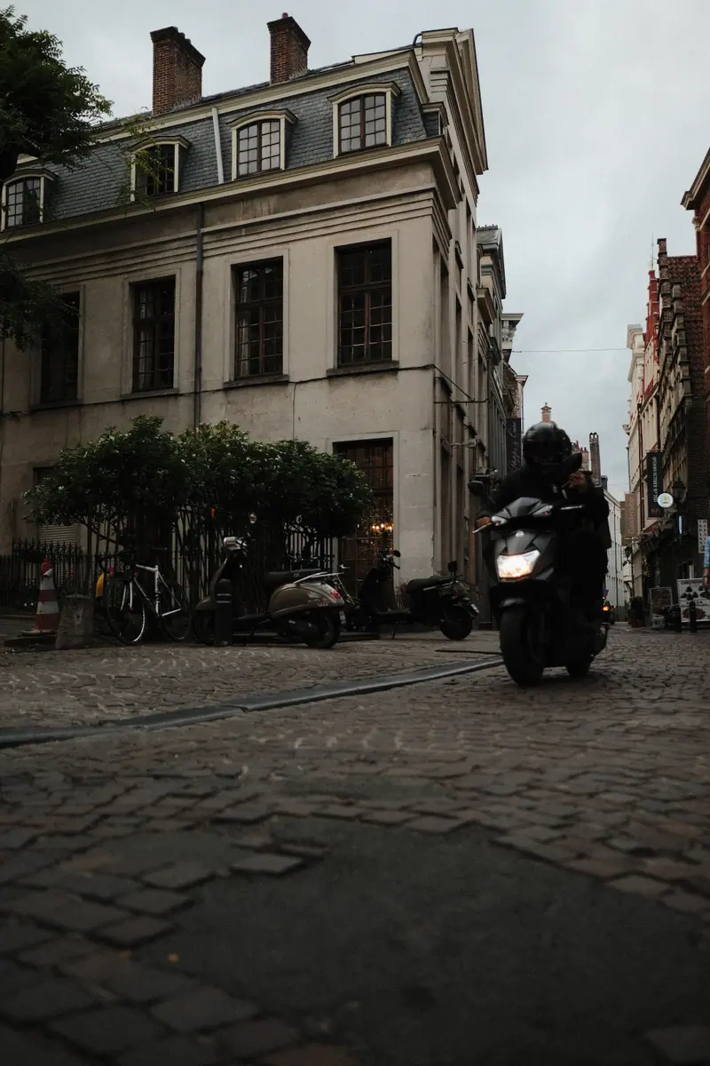 A scooter rider rounds a cobbled corner beside a grand grey townhouse